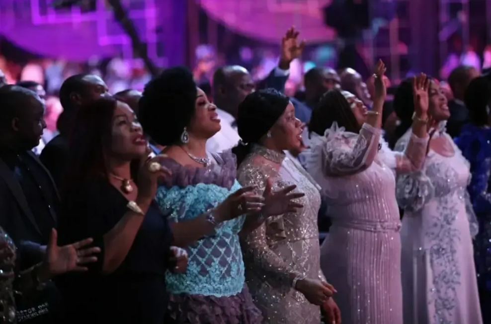 Five African women in beautiful gowns stand and sing along at Praise Night with Pastor Chris.